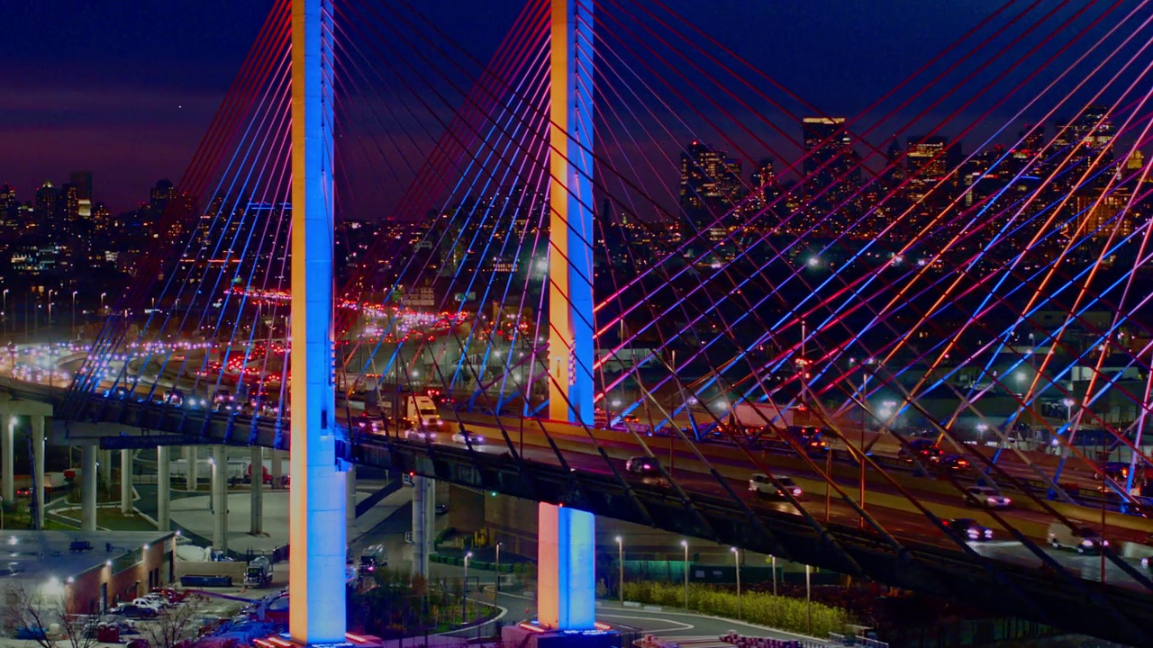 深夜的车流在灯火通明的科斯丘什科大桥(Kosciuszko Bridge)上行驶，背景是曼哈顿和布鲁克林的远景。航拍视频与快速长全景轨道相机运动。