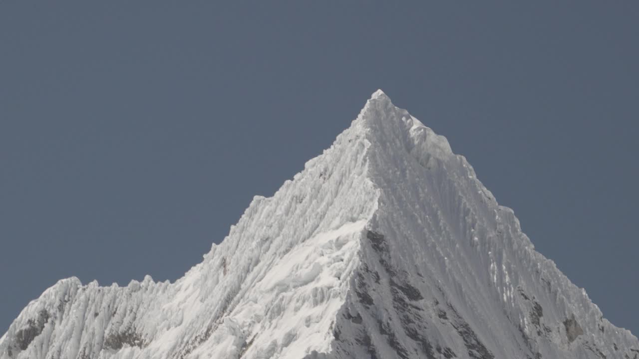 在秘鲁华斯卡兰的白科迪勒拉安第斯山脉的高山上，拉古纳帕隆泻湖的一座金字塔形山的冰川被冰雪覆盖，阳光明媚的日子里，山峰被白雪覆盖。