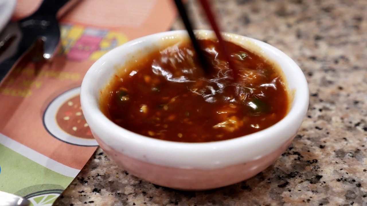 在泰国曼谷的一家餐馆里，用筷子在一个小蘸碗里混合一些辛辣的寿喜烧酱。