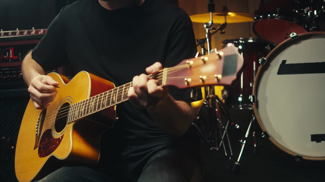 一名年轻的音乐家坐在录音室的音乐设备中间弹着原声吉他。吉他手演奏旋律