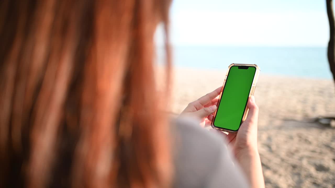 沙滩上的女人拿着绿屏手机