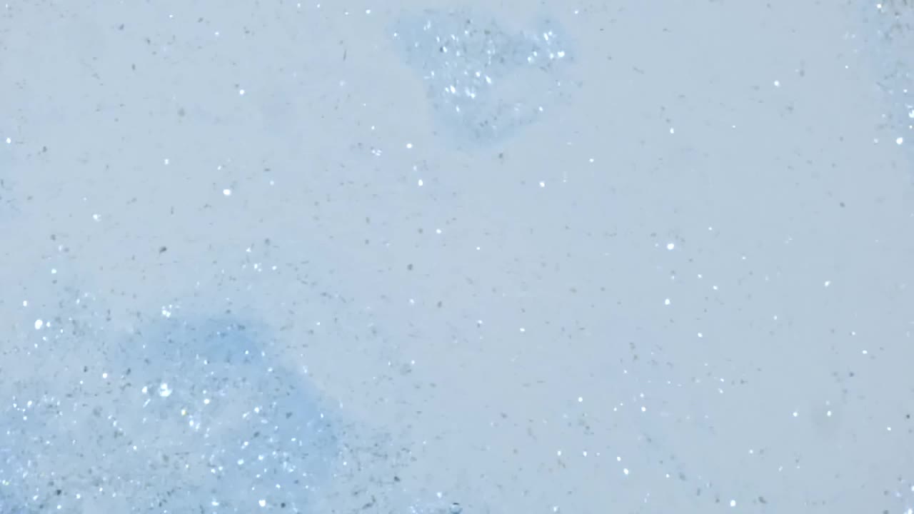 微距拍摄的粉末制成的黄金颗粒，化妆纹理在水中下降在白色的背景。缓慢的运动。天然化妆品的生产
