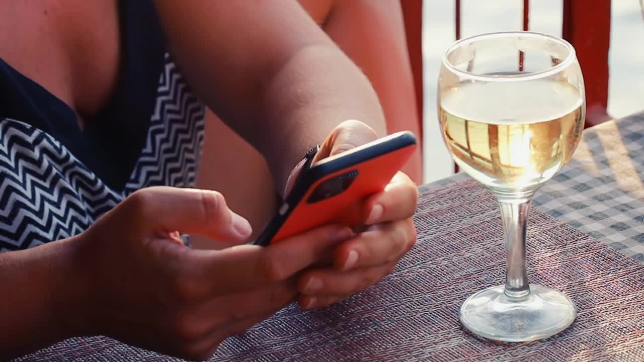 夕阳下，手持手机和酒杯的女人
