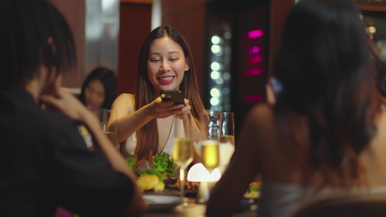 年轻漂亮的亚洲女子在酒吧用餐前用手机拍下食物。