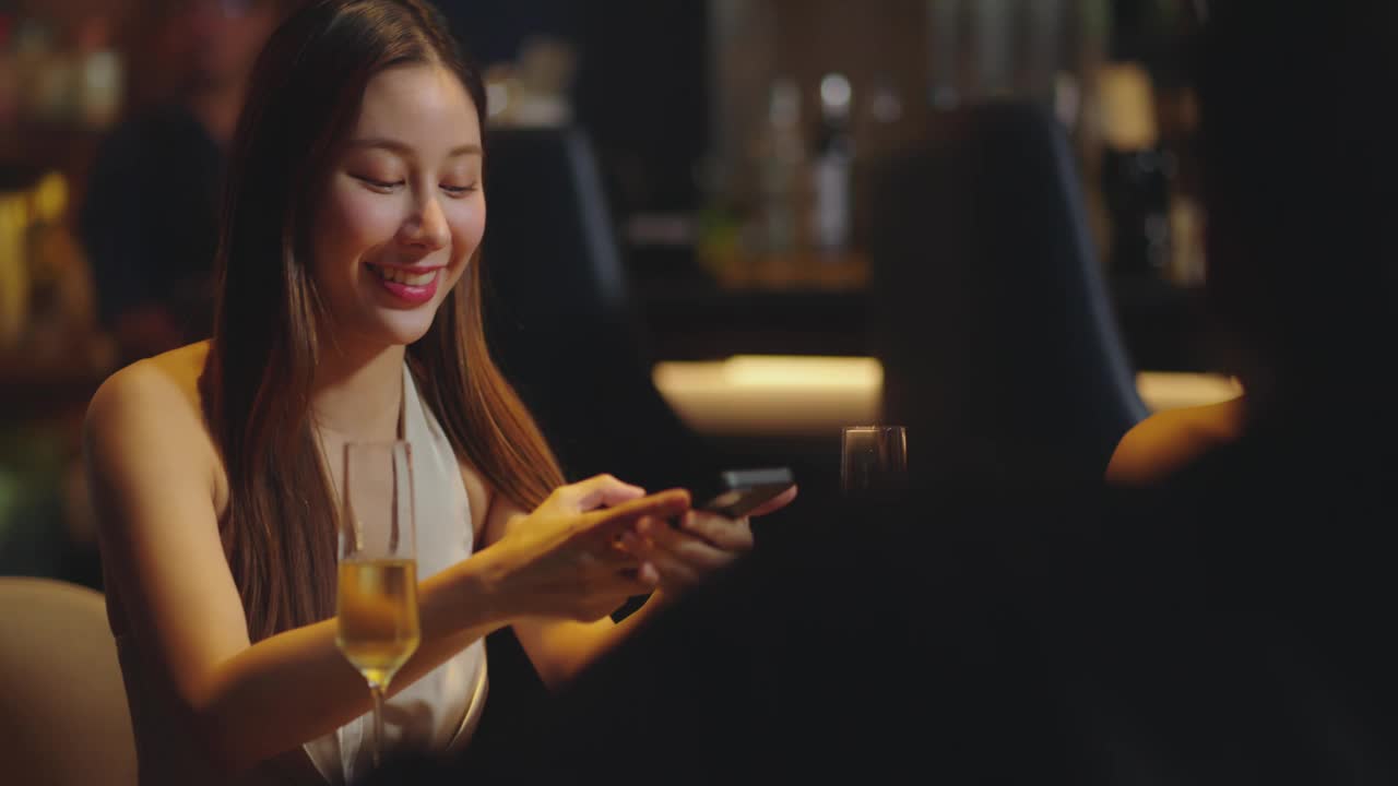 年轻漂亮的亚洲女子在酒吧用餐前用手机拍下食物。