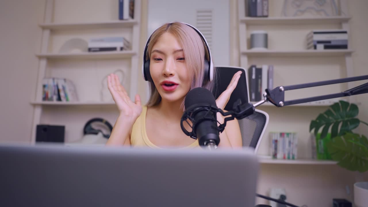 詳情圖-亞洲年輕的音頻DJ女士對(duì)著麥克風(fēng)講話。迷人美麗的女性博主影響者戴著耳機(jī)，在家庭工作室為電臺(tái)錄制早間新聞播客節(jié)目。