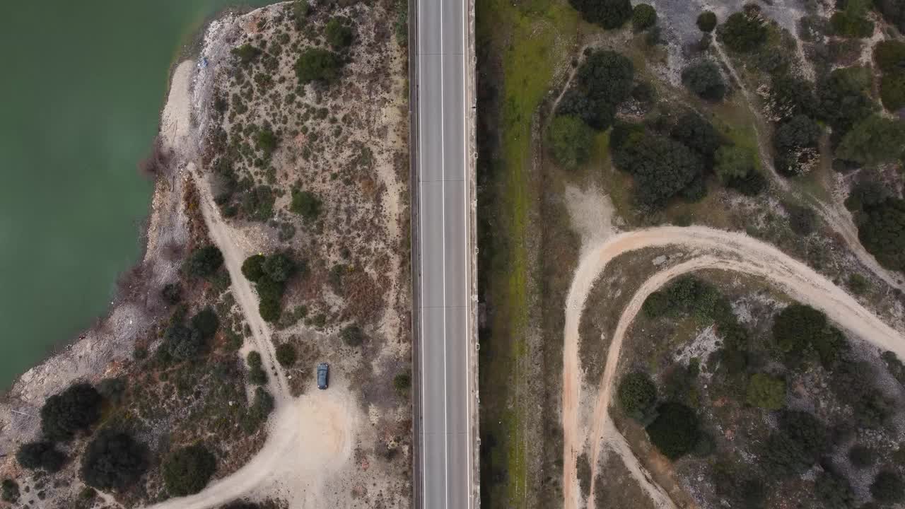 这是一架无人机在农村地区拍摄的一条道路，道路的一边是湖泊，另一边是树林，一辆蓝色的汽车沿着道路行驶