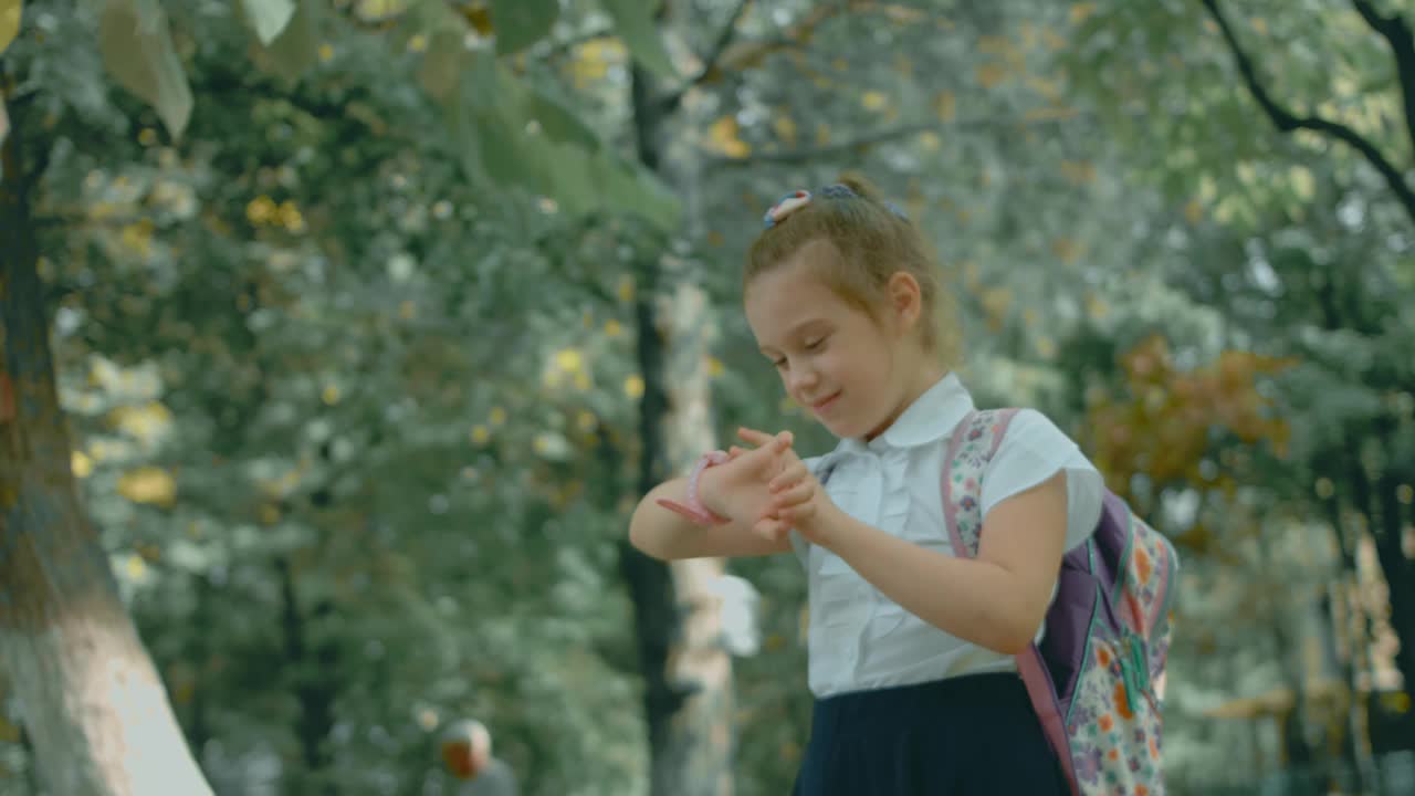 美丽的白人女学生下课后在学校公园户外使用智能手表。快乐的孩子在智能手机上与父母视频通话。带GPS追踪器的智能手表。