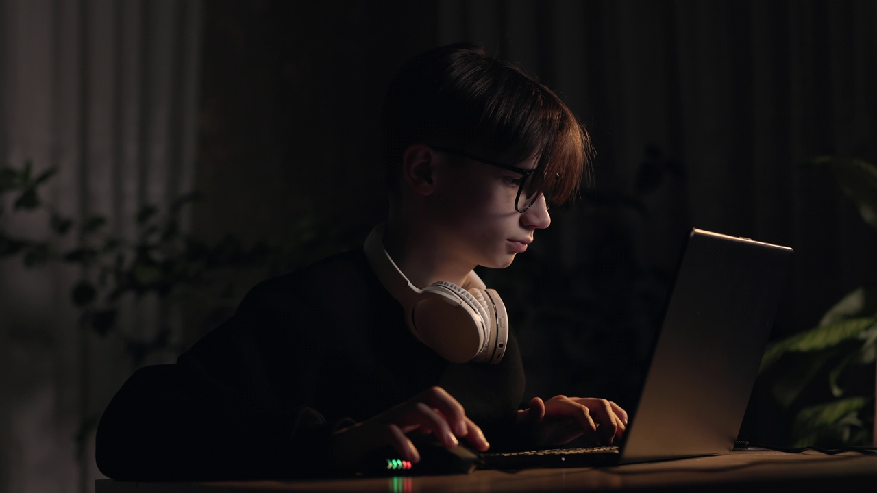 电子游戏赌博成瘾。一个专注的少年在黑暗的房间里用鼠标和键盘玩电脑射击视频游戏、电子竞技、虚拟比赛。网络视频游戏技术概念。