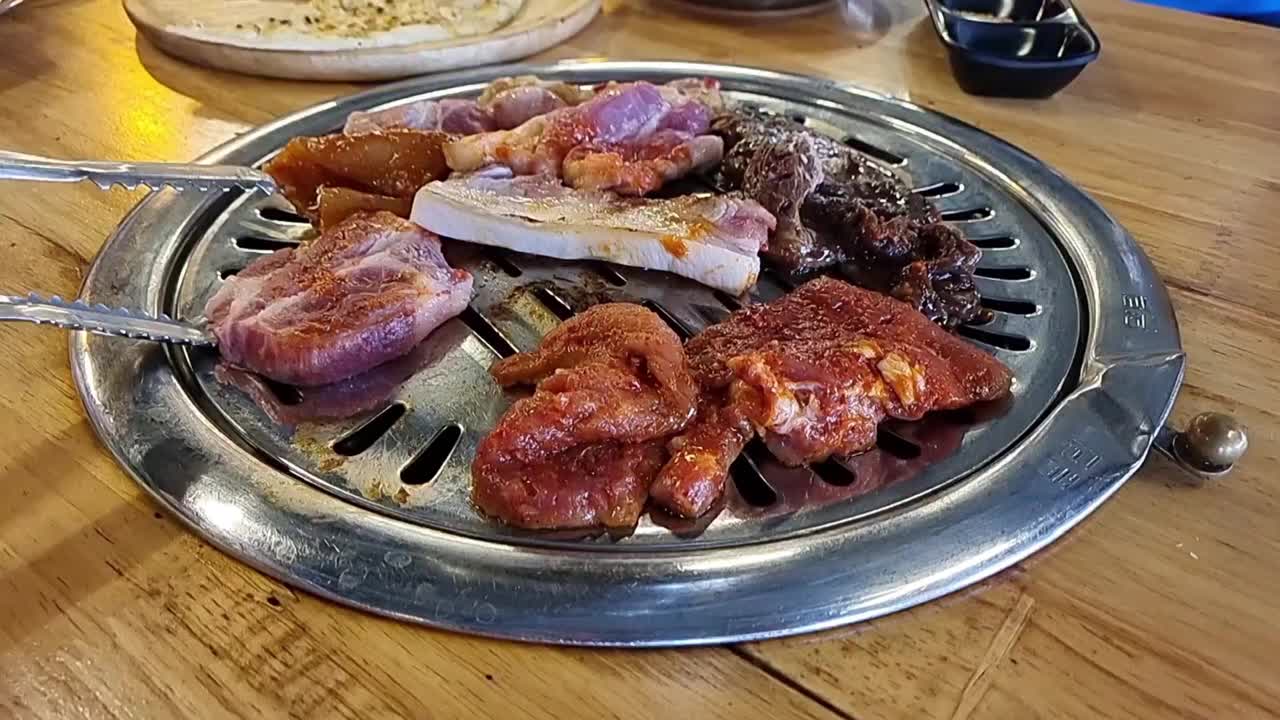 在韩国餐厅吃烧烤。熏肉，五花肉，牛肉在木炭烤架上烤。