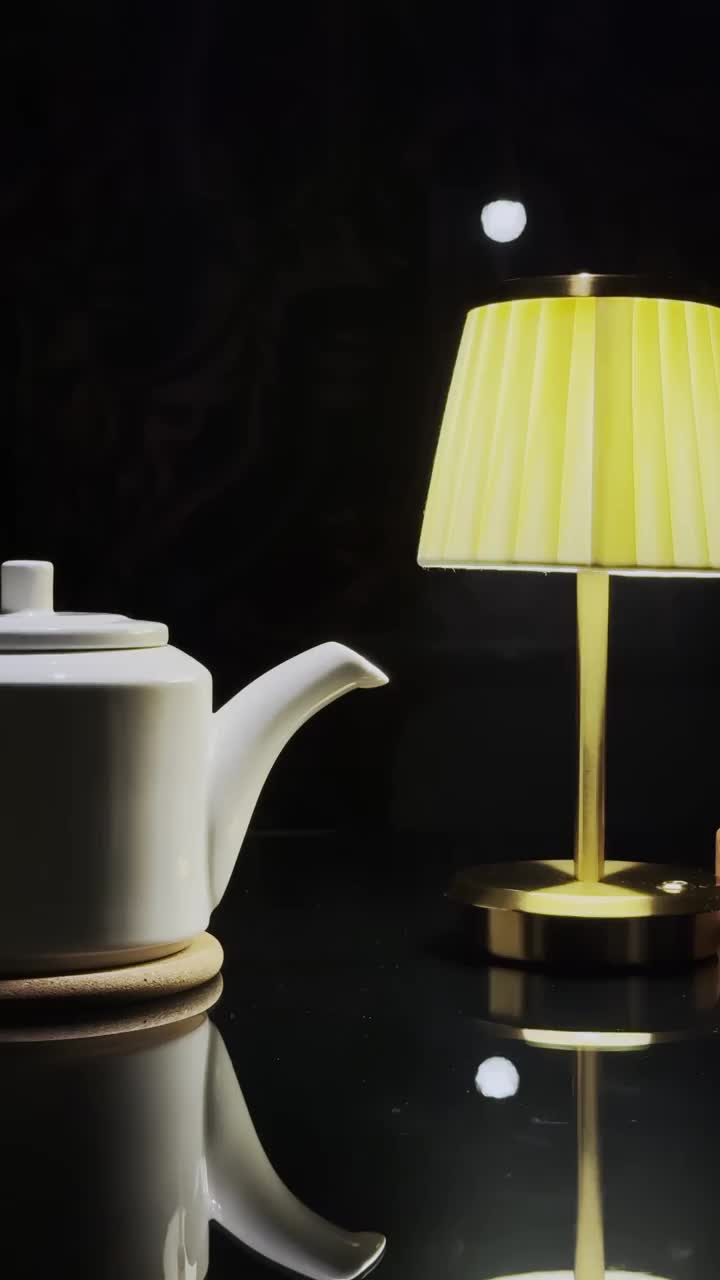 一个白色的茶壶立在黑色镜面的桌子上，在黑暗的背景下，旁边是一盏台灯或落地灯。