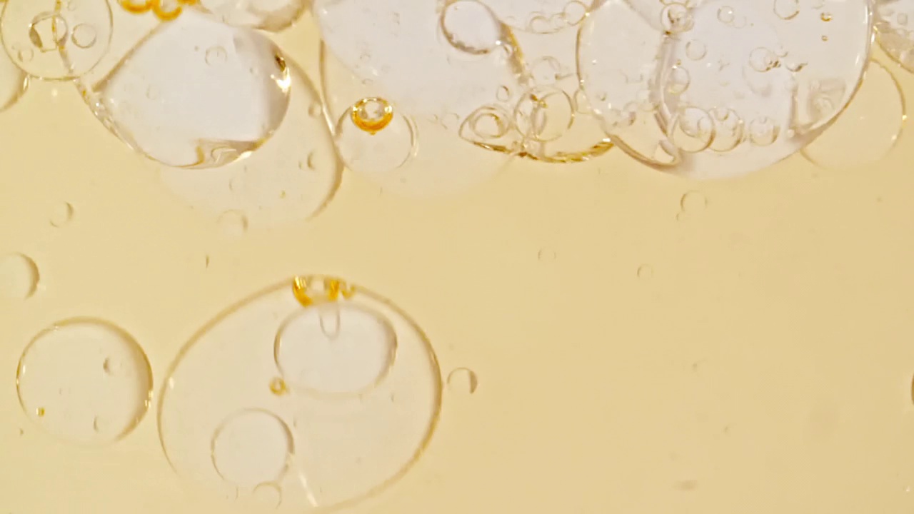 慢动作移动的金黄油，气泡在水中上升在浅白色的背景。带有气泡的透明化妆品凝胶液。微距镜头。