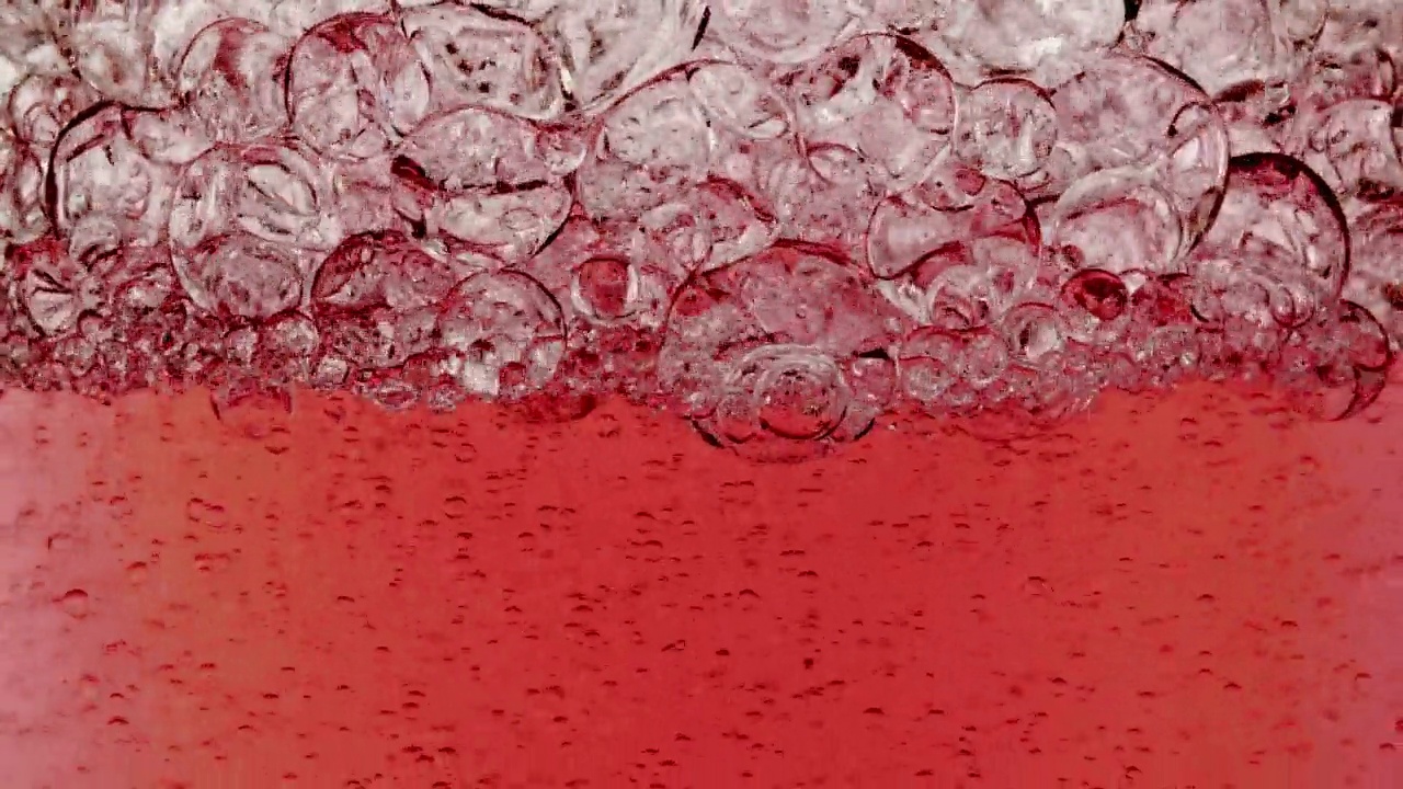 缓慢移动的红油，气泡在水中上升的白色背景。带有气泡的透明化妆品凝胶液。微距镜头。