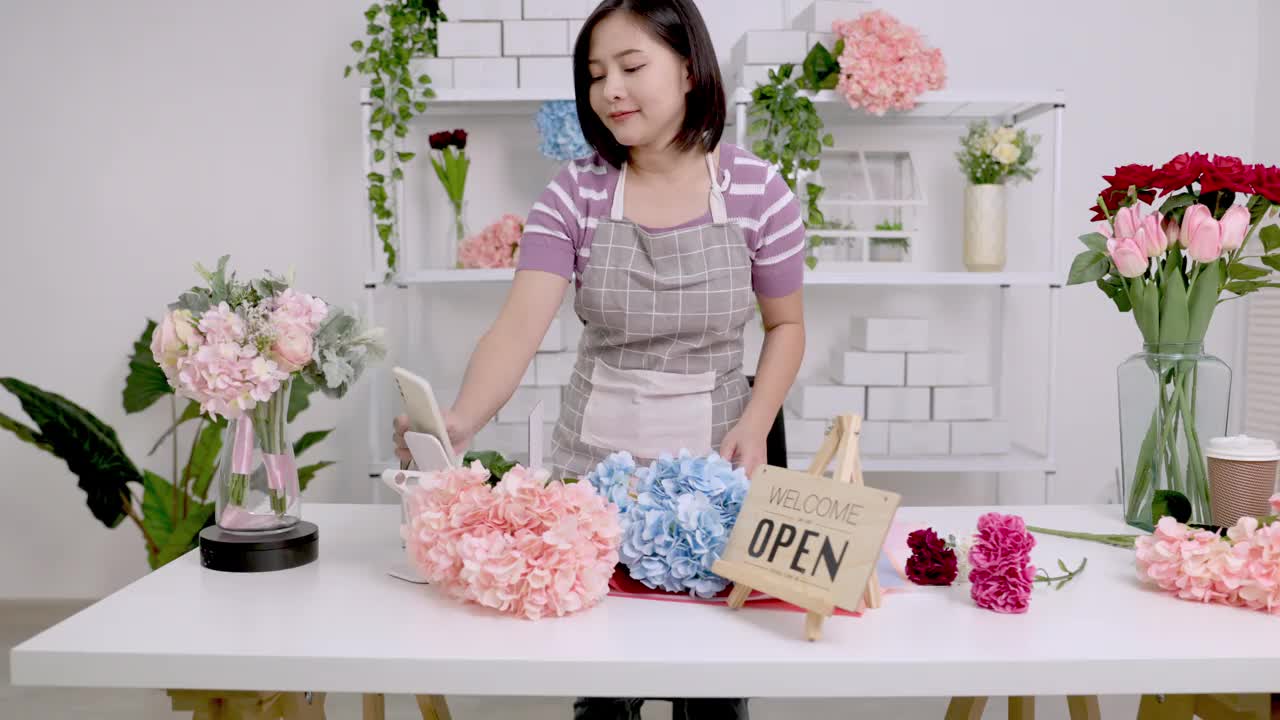 亚洲男性网红或中小企业老板们微笑着用家用摄像机自拍。微笑的女花商在打电话。年轻女子在商店工作，牌子上写着“开门”。