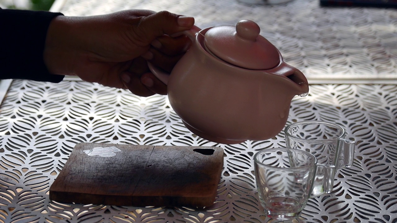 详情图-一只手从玻璃茶壶里把茶倒在木制托盘上