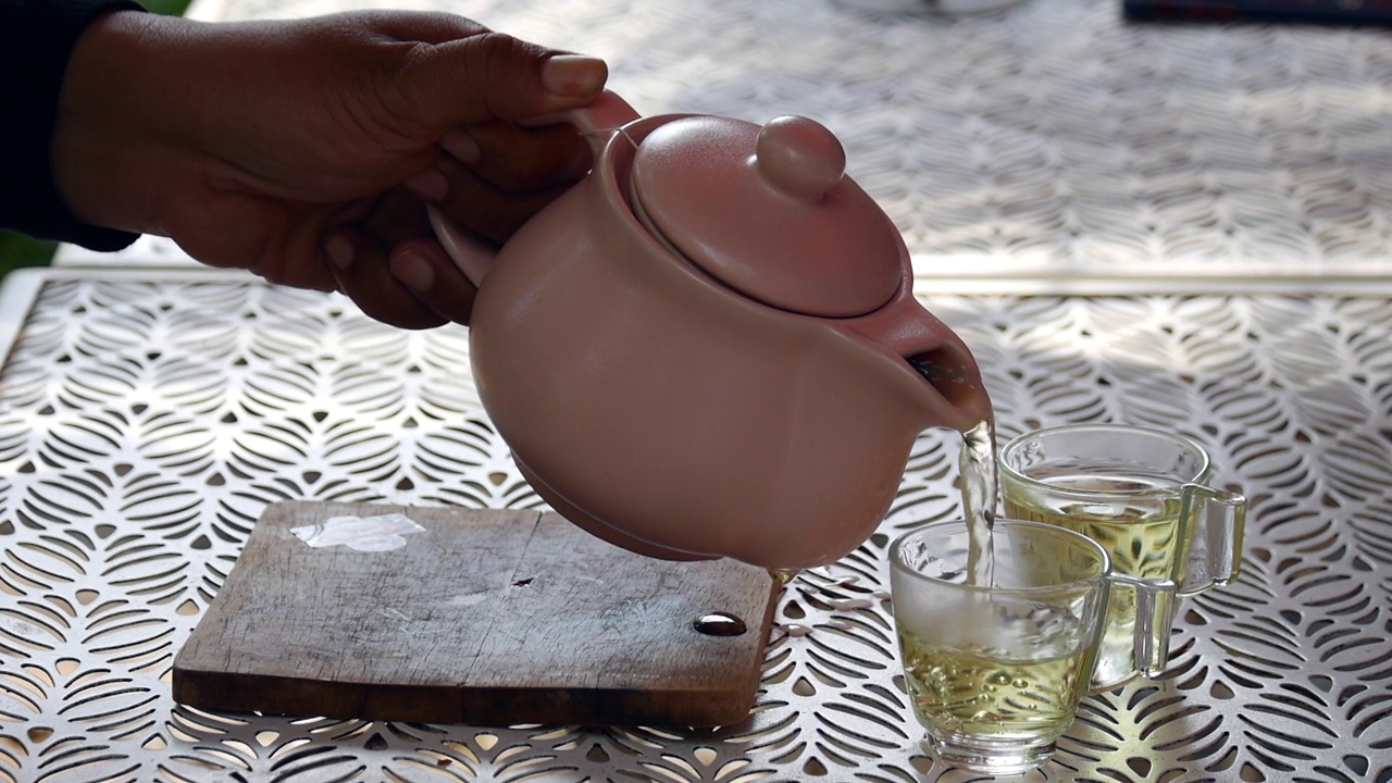 详情图-一只手从玻璃茶壶里把茶倒在木制托盘上