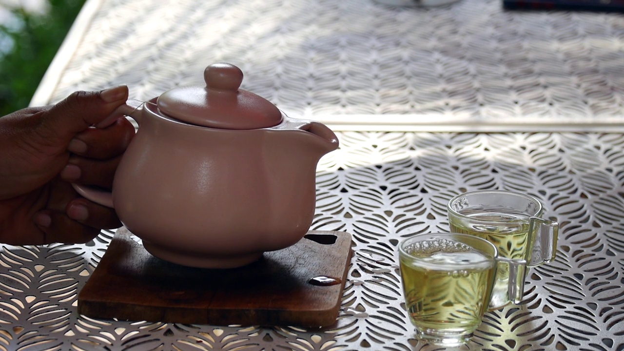 详情图-一只手从玻璃茶壶里把茶倒在木制托盘上
