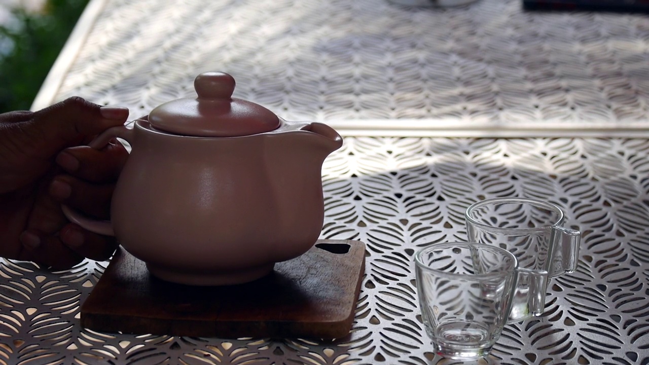 详情图-一只手从玻璃茶壶里把茶倒在木制托盘上