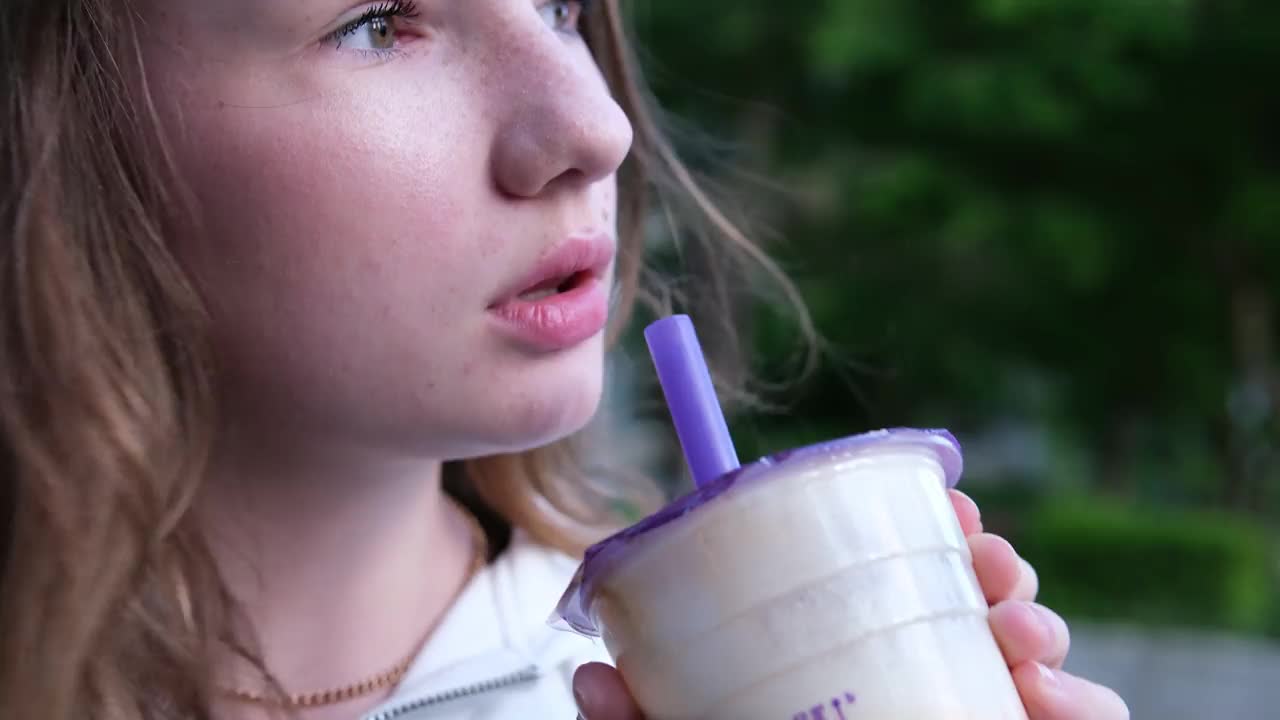 美味的饮料奶茶喝着美味的咖啡茶冰沙在街上一个年轻的女孩高兴地从一根稻草中抽出液体咀嚼吞咽雅米雅米。