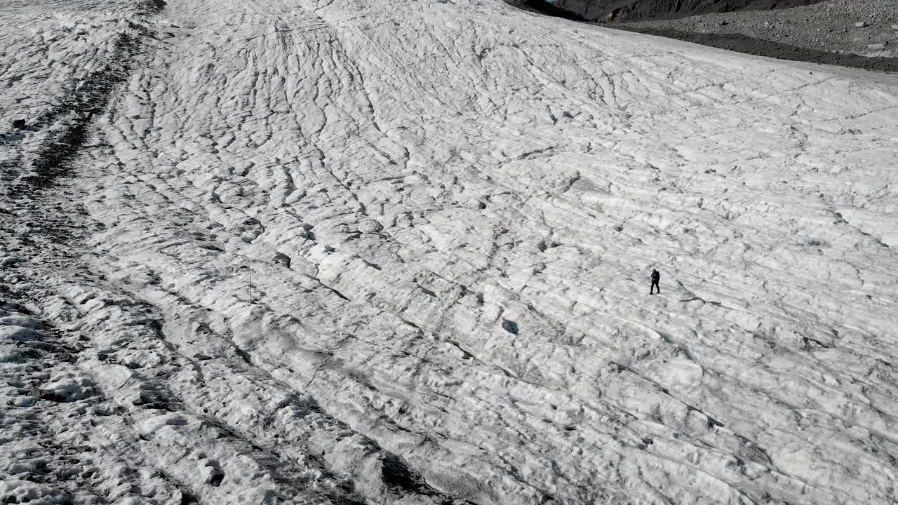 在瑞士瓦莱州萨斯费附近的Allalin冰川上，一名徒步旅行者从空中飞过，阳光从瑞士阿尔卑斯山的山峰后面照过来