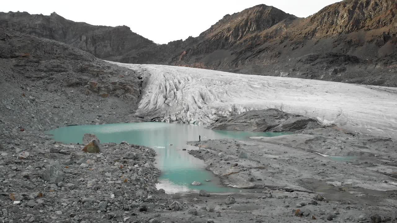 在瑞士瓦莱州萨斯费附近Hohlaub冰川的绿松石冰川湖岸，一架飞机飞过一名徒步旅行者