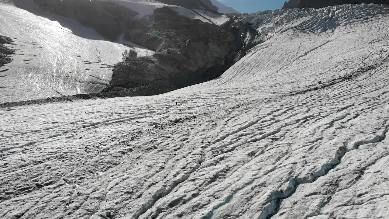 在瑞士阿尔卑斯山的一个阳光明媚的日子里，一名徒步旅行者和一名登山者在瓦莱州萨斯费附近的Allalin冰川上走过冰并跳过裂缝