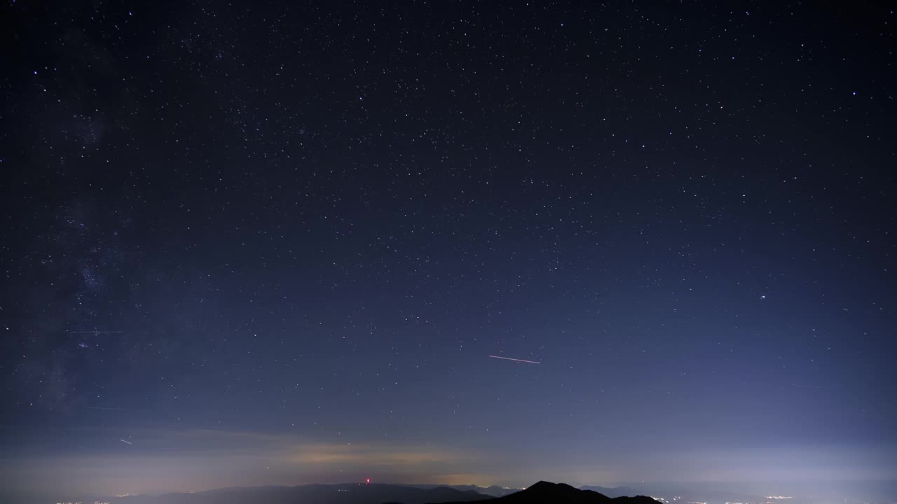 银河，星空，山峰的剪影和夜晚城市的灯光