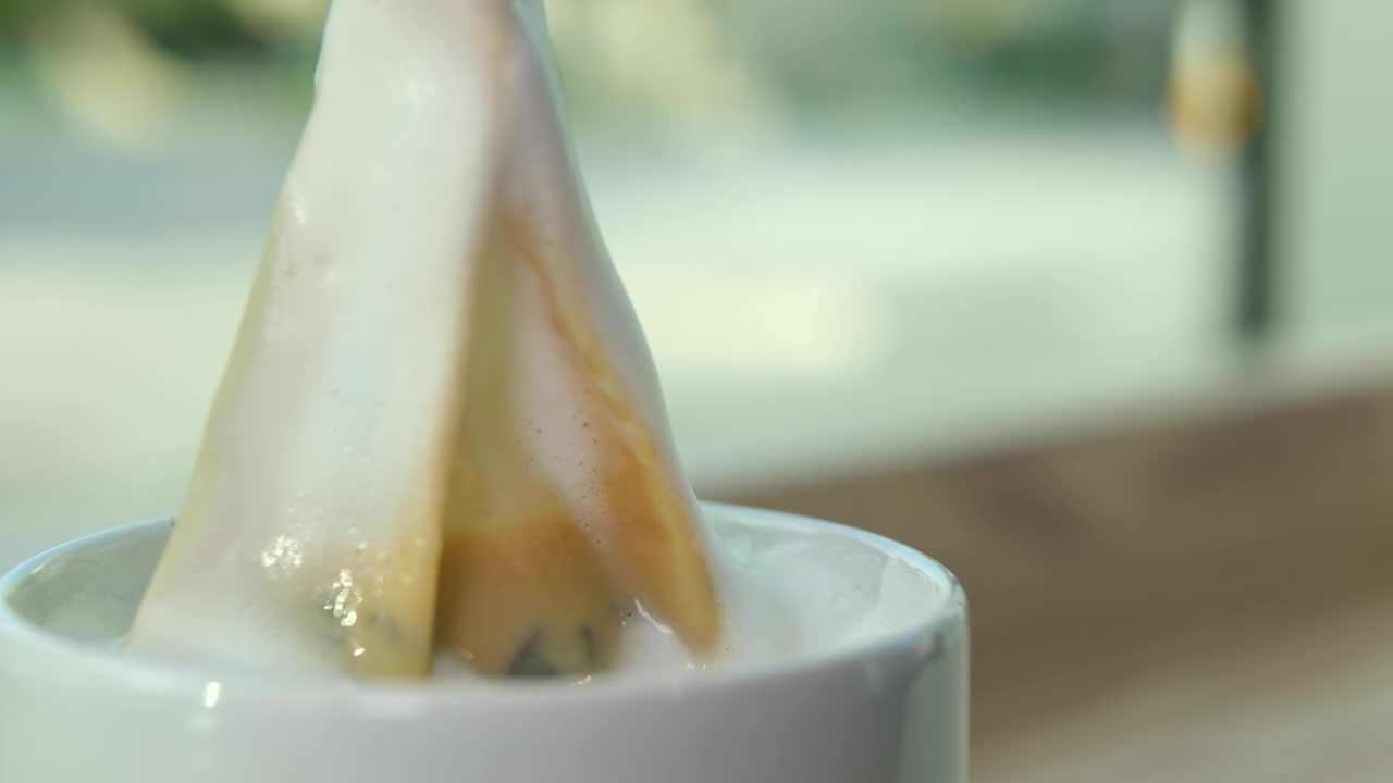详情图-奶茶，一袋袋草本绿茶从白色的杯中提起，美味的饮品流到桌上，奶沫、鲜奶油的近景，利于感冒、暖身、饮热腾腾的灵丹妙药