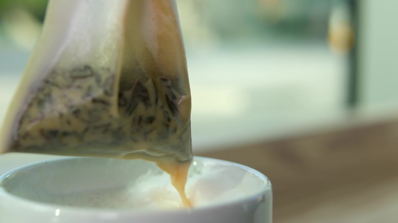详情图-奶茶，一袋袋草本绿茶从白色的杯中提起，美味的饮品流到桌上，奶沫、鲜奶油的近景，利于感冒、暖身、饮热腾腾的灵丹妙药