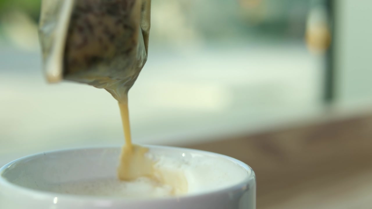 详情图-奶茶，一袋袋草本绿茶从白色的杯中提起，美味的饮品流到桌上，奶沫、鲜奶油的近景，利于感冒、暖身、饮热腾腾的灵丹妙药