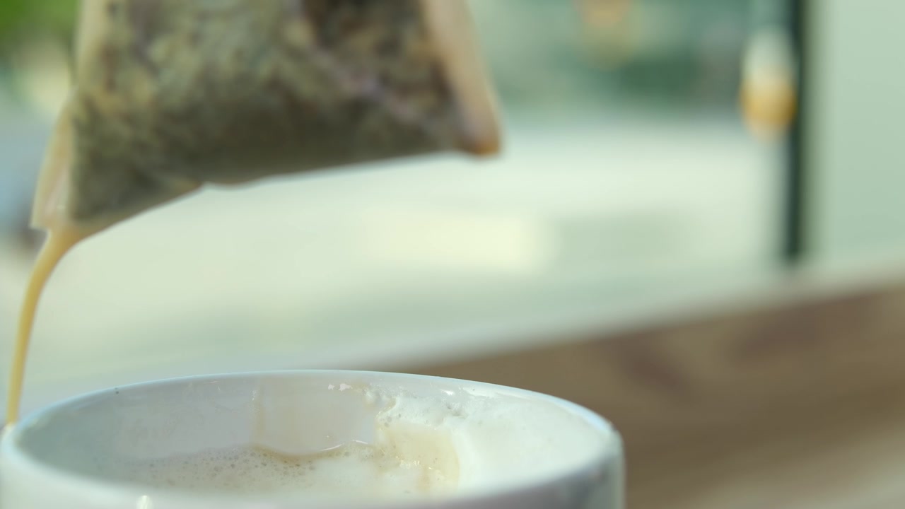 详情图-奶茶，一袋袋草本绿茶从白色的杯中提起，美味的饮品流到桌上，奶沫、鲜奶油的近景，利于感冒、暖身、饮热腾腾的灵丹妙药