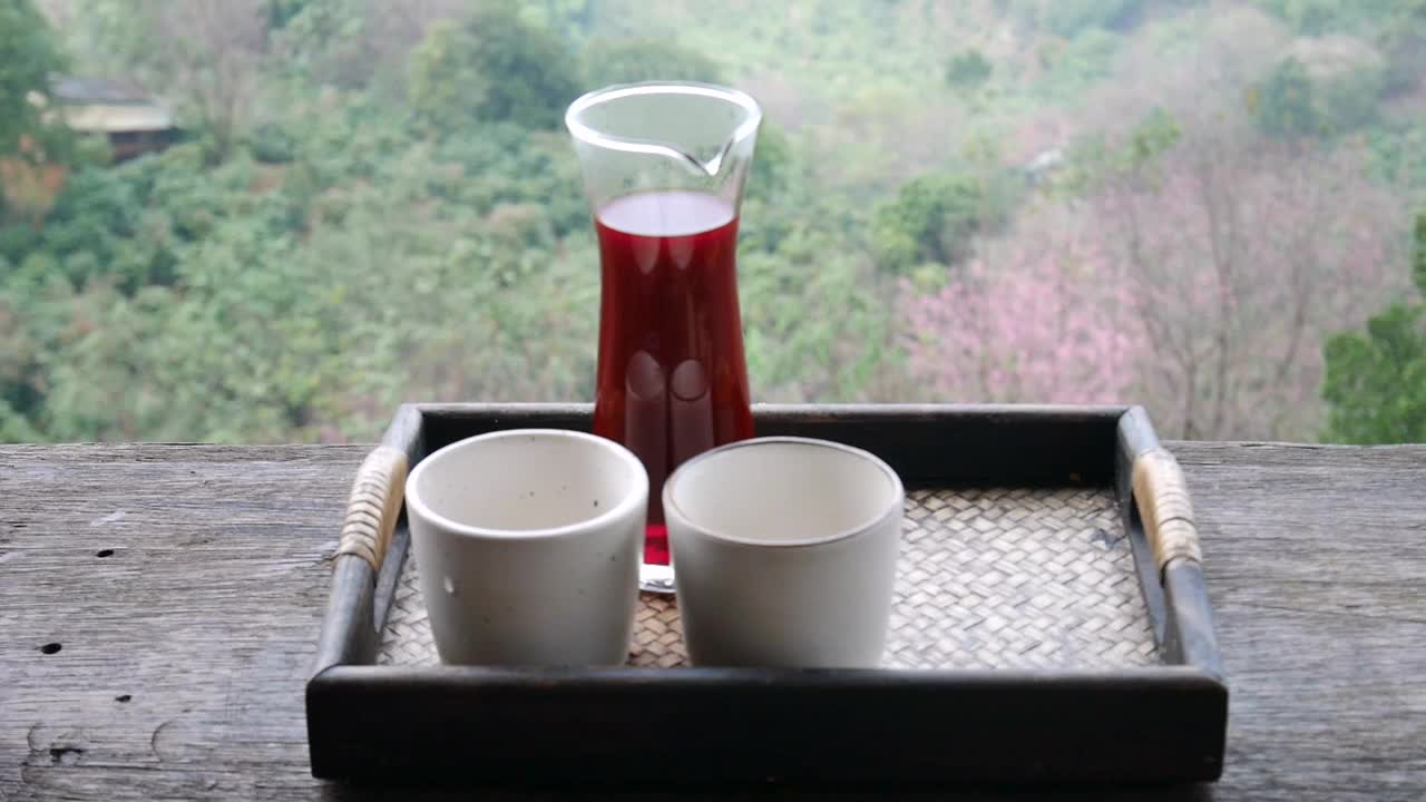 一只手从玻璃茶壶里把茶倒在木制托盘上