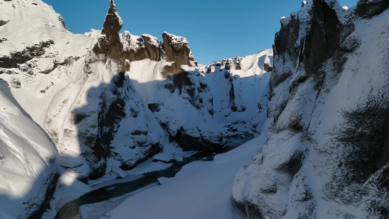 在一个阳光明媚的日子里，鸟瞰图穿过一个冰雪覆盖的峡谷，在冰川河流上流动