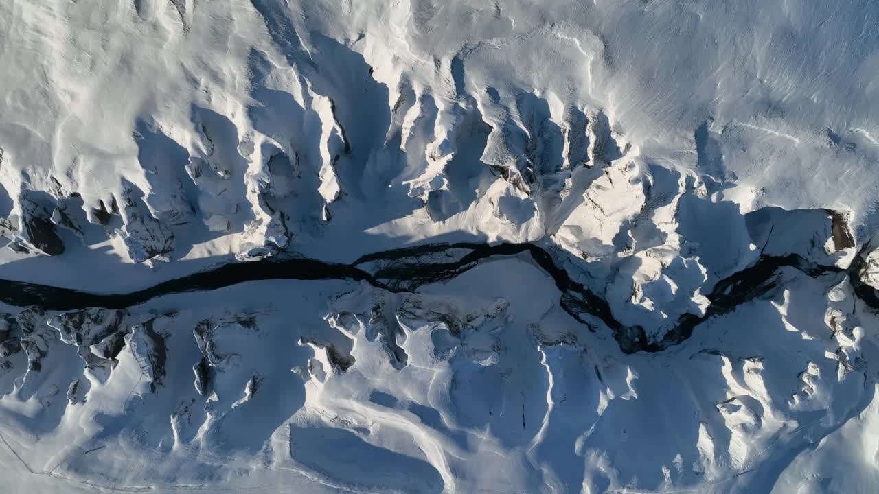 在一个阳光明媚的日子里，从空中俯瞰一条冰川河流流经被雪覆盖的峡谷