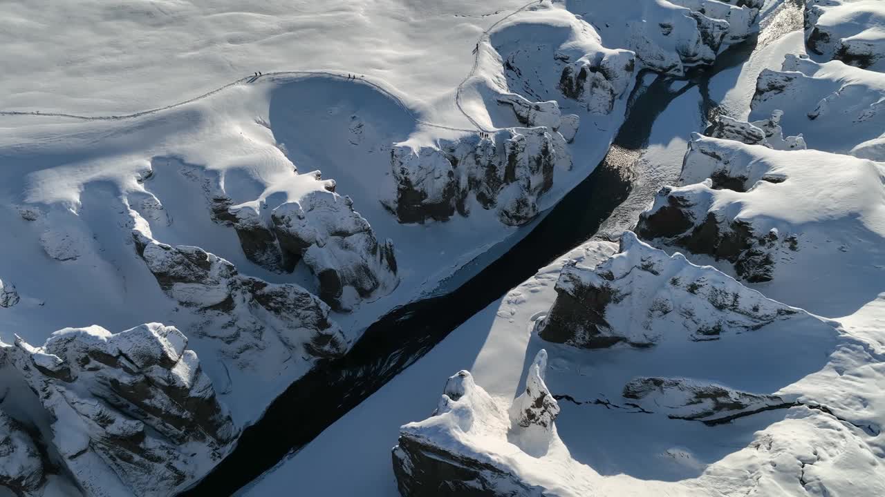 在一个阳光明媚的夜晚，从空中俯瞰冰川河流流经被雪覆盖的峡谷