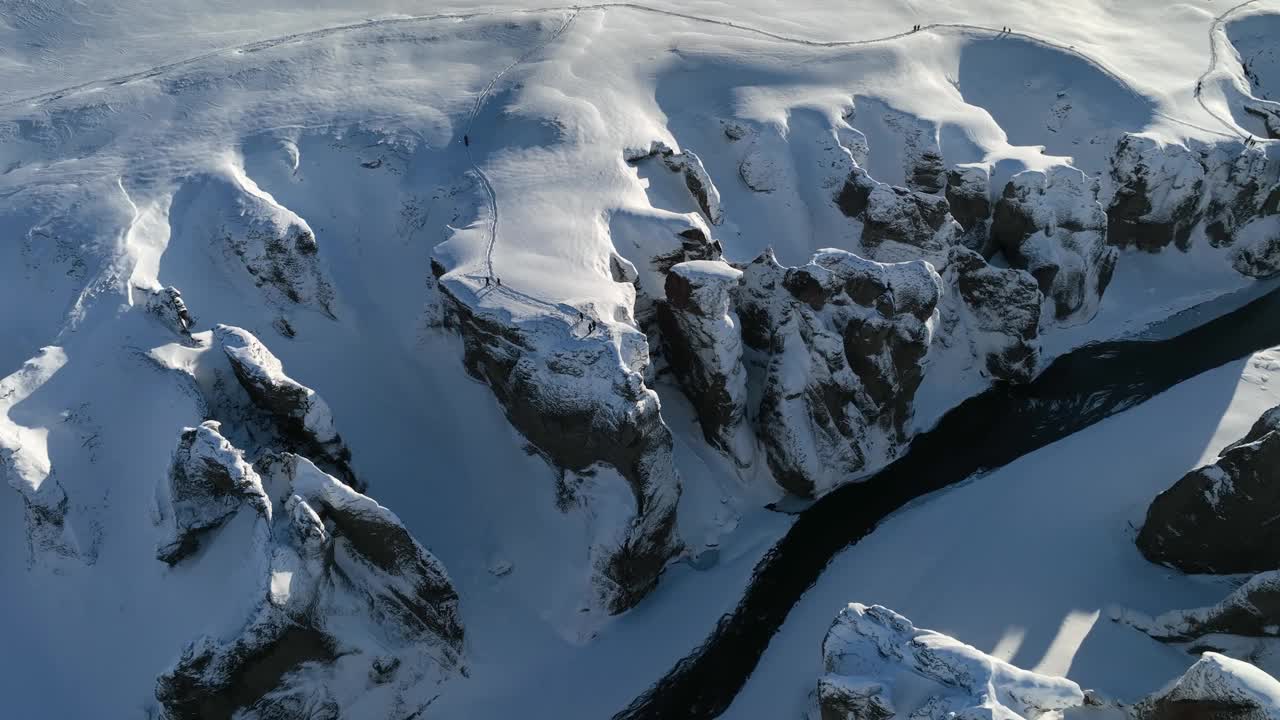 在一个阳光明媚的日子里，从空中俯瞰一条冰川河流流经被雪覆盖的峡谷