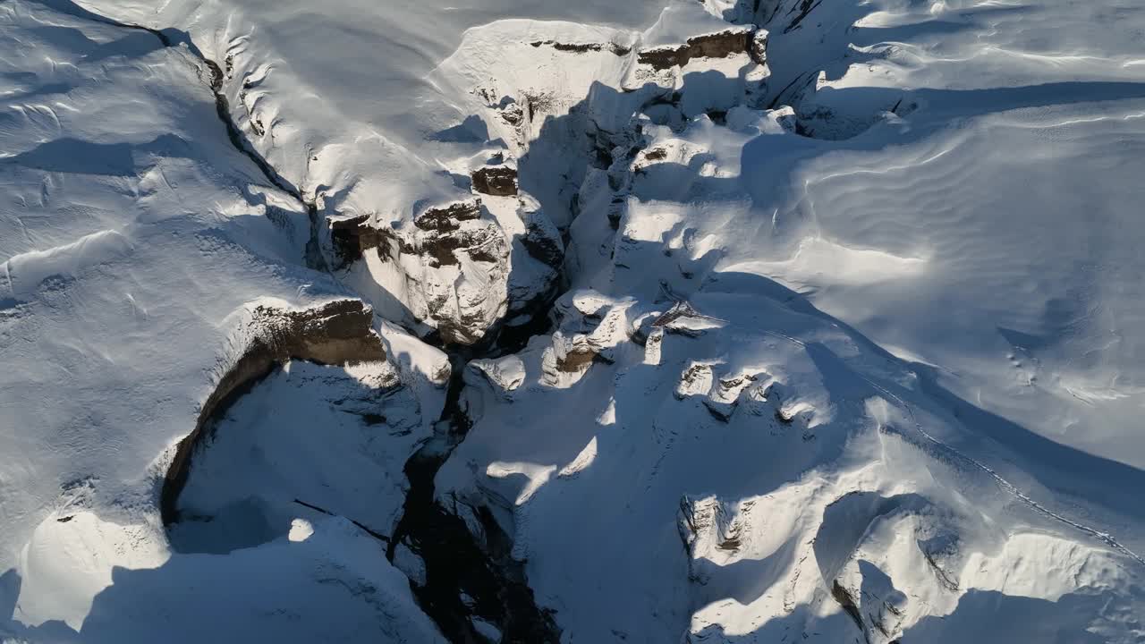 在一个阳光明媚的日子里，从空中俯瞰冰川河流流经被雪覆盖的峡谷