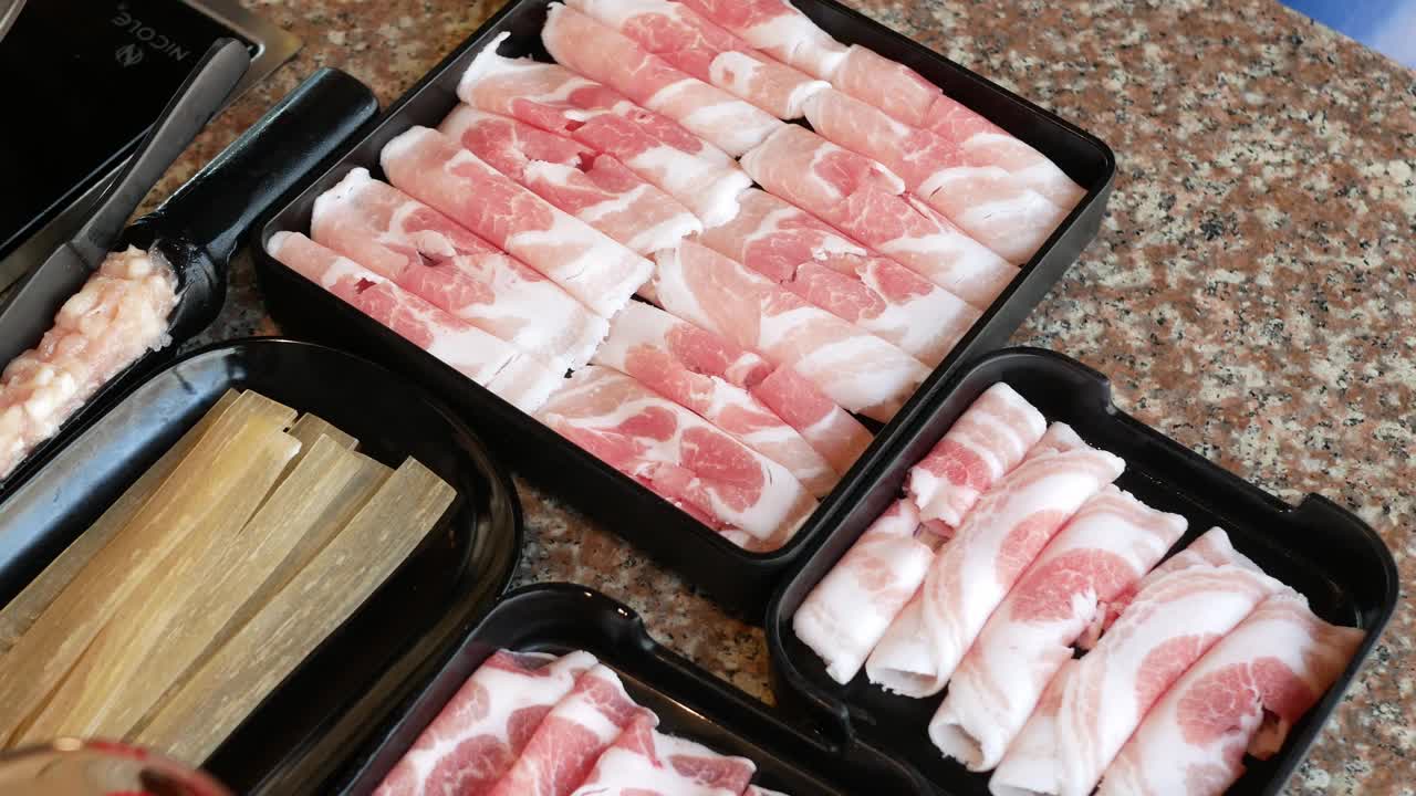 托盘里的猪肉牛肉片、腌肉和中式干面摆上餐桌，准备烹制中式四川风味火锅，合家欢用餐。