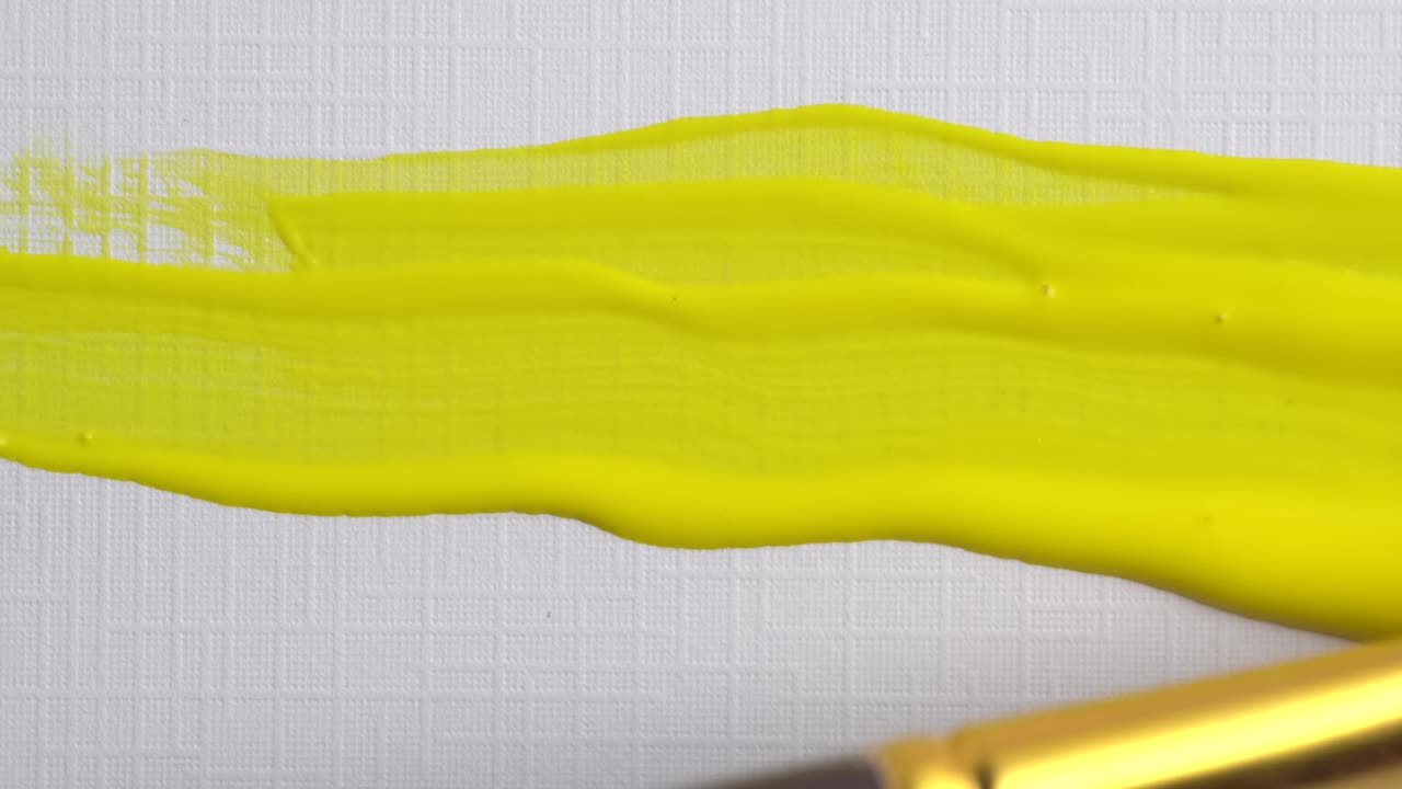 艺术家手持画笔绘制油画的特写。在帆布上画淡紫色和黄色的线条。艺术家用紫色丙烯酸颜料作画