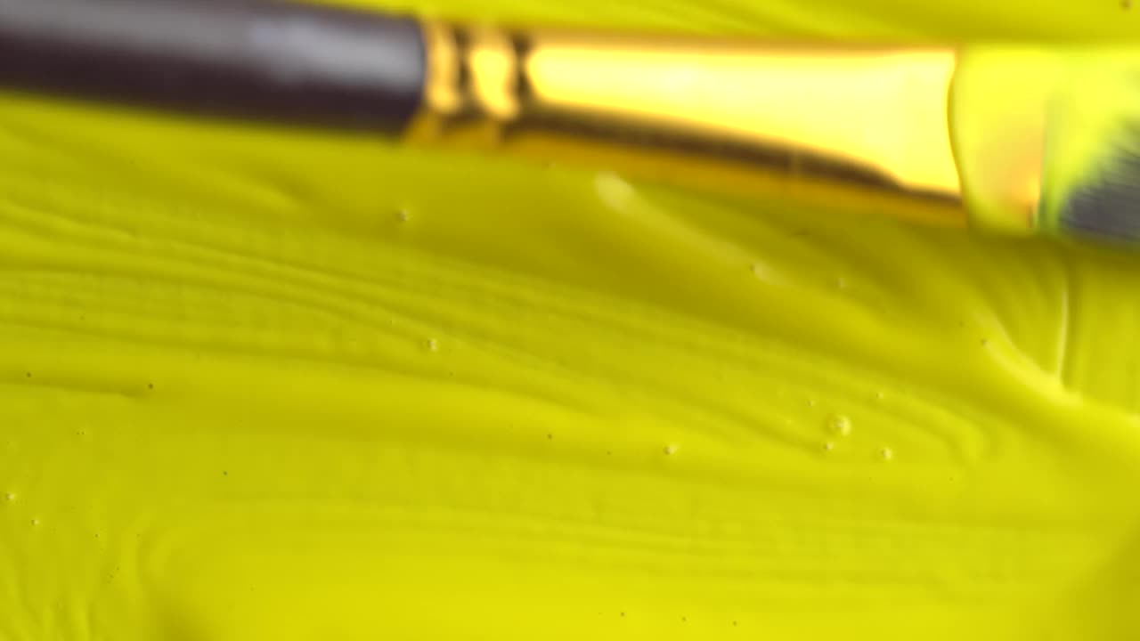 艺术家手持画笔绘制油画的特写。在帆布上画淡黄色的线条。艺术家用黄色丙烯酸颜料作画