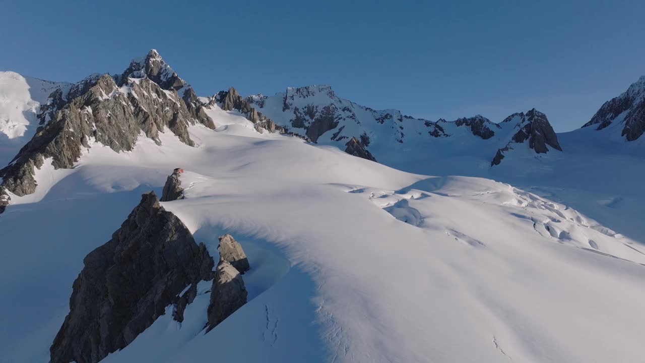 在雪山和冰川之间的一个偏远的野生小屋避难所。壮丽的地形在一个美丽的一天，因为太阳落在这个北极冰冻的世界。巨大的裂缝将大地一分为二。无人机的空中。