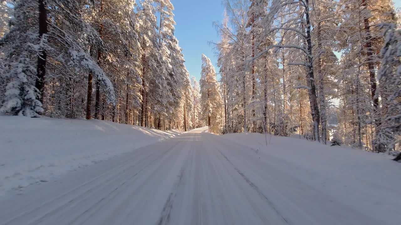 POV风景优美的冬季驾驶在冰雪覆盖的阳光亲吻芬兰森林