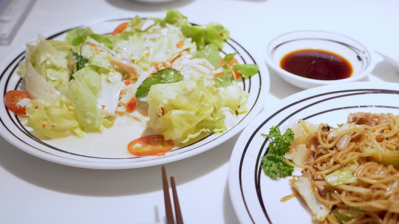 在餐馆里从左到右翻炒一餐，一盘沙拉、炒面和煎饺子。