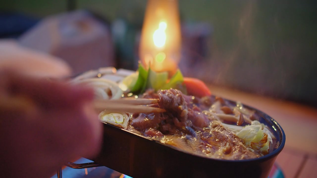 詳情圖-一個(gè)人用筷子享用美味火鍋的特寫(xiě)，背景是溫暖的燭光