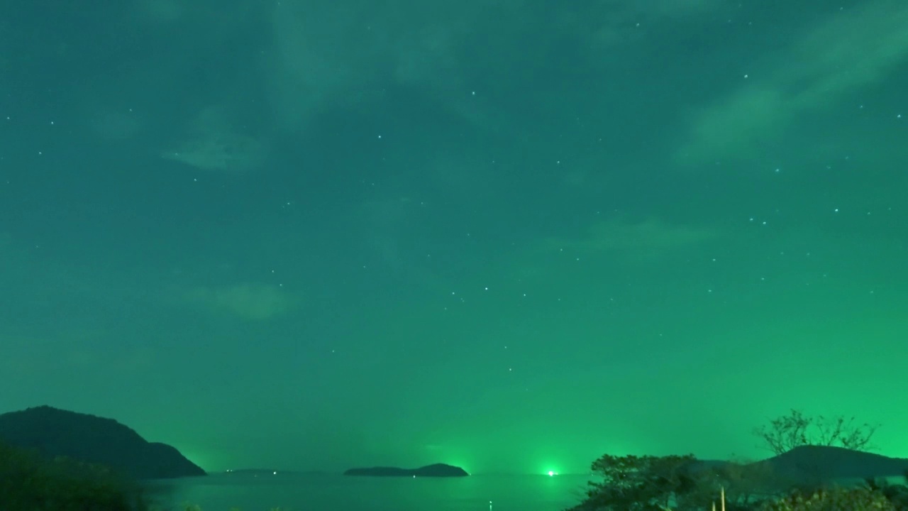 泰国普吉岛，夜晚的星空和绿色的星光在平静的海浪和海水中与渔船在一起