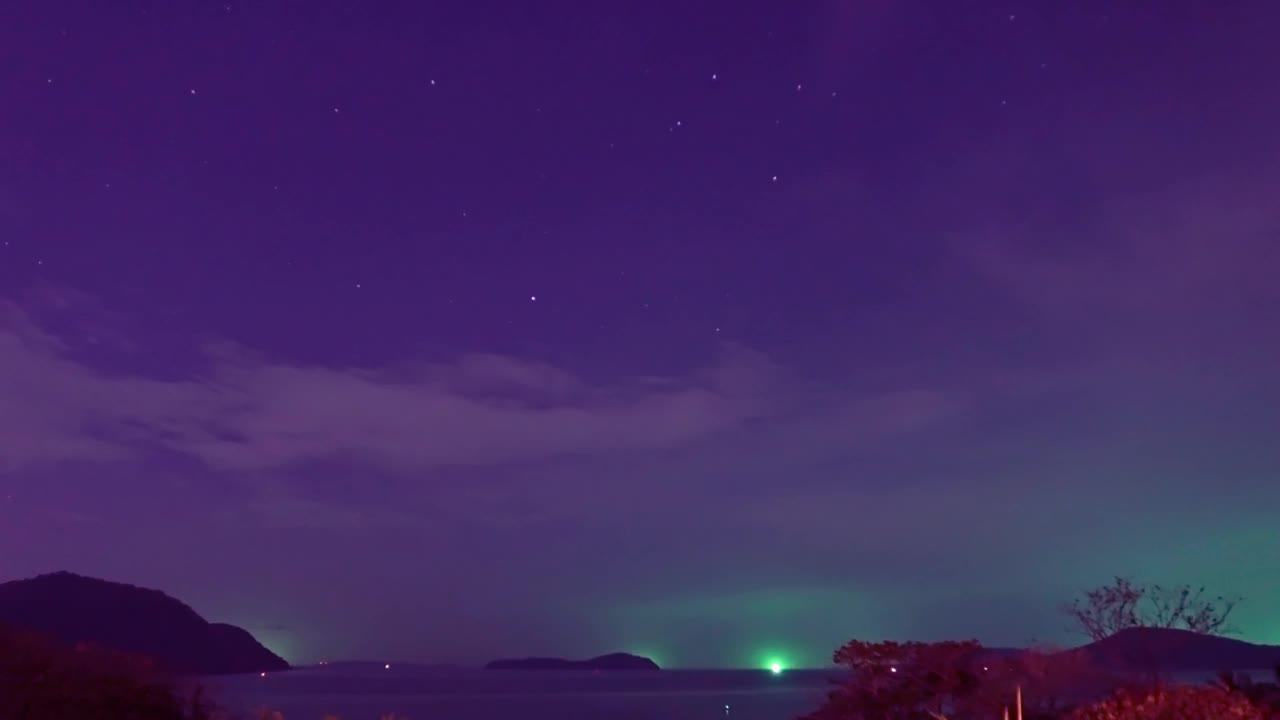 明亮的绿色星光在品红星空在平静的海浪和海水与剪影山岛在森林的夜空