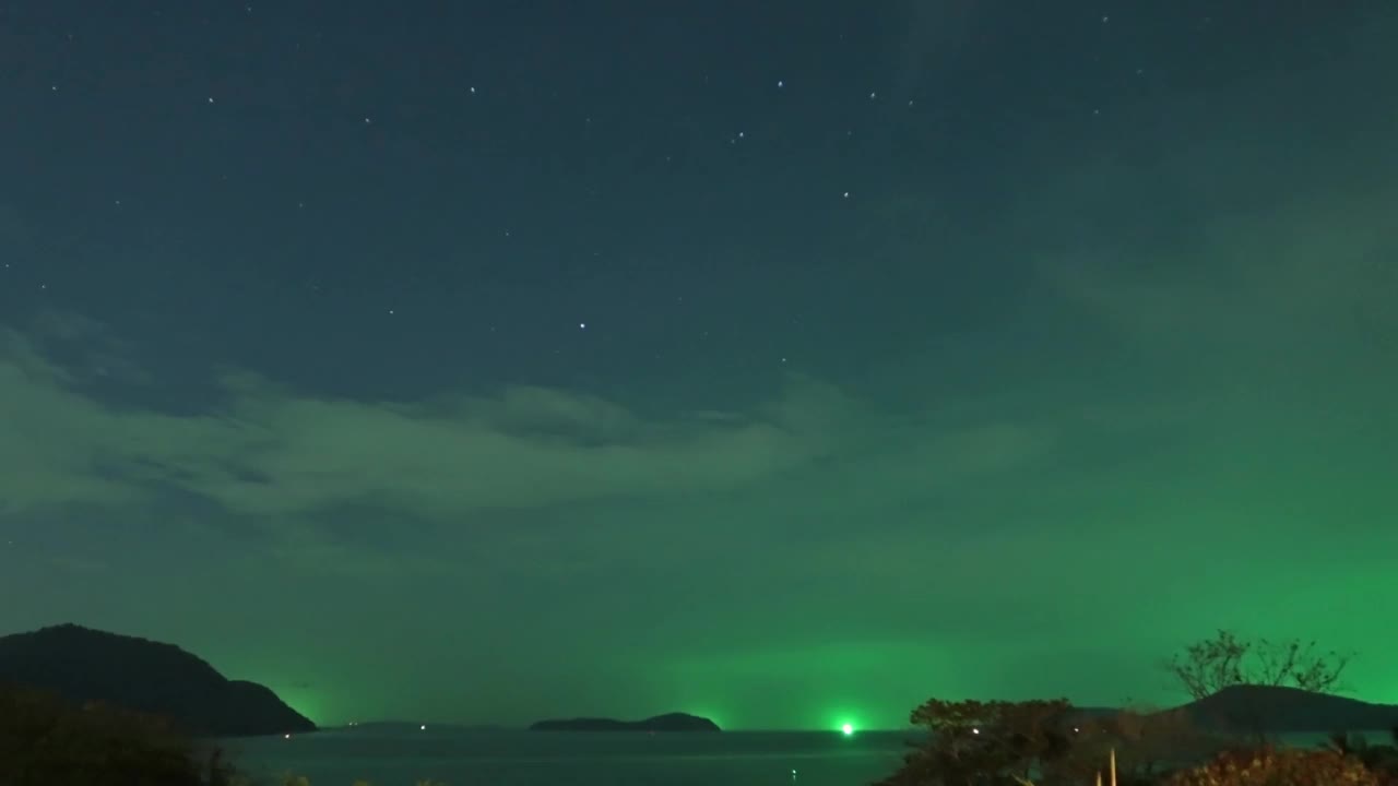 明亮的绿色星光在深蓝色的星空上，在平静的海洋海水中轮廓山林