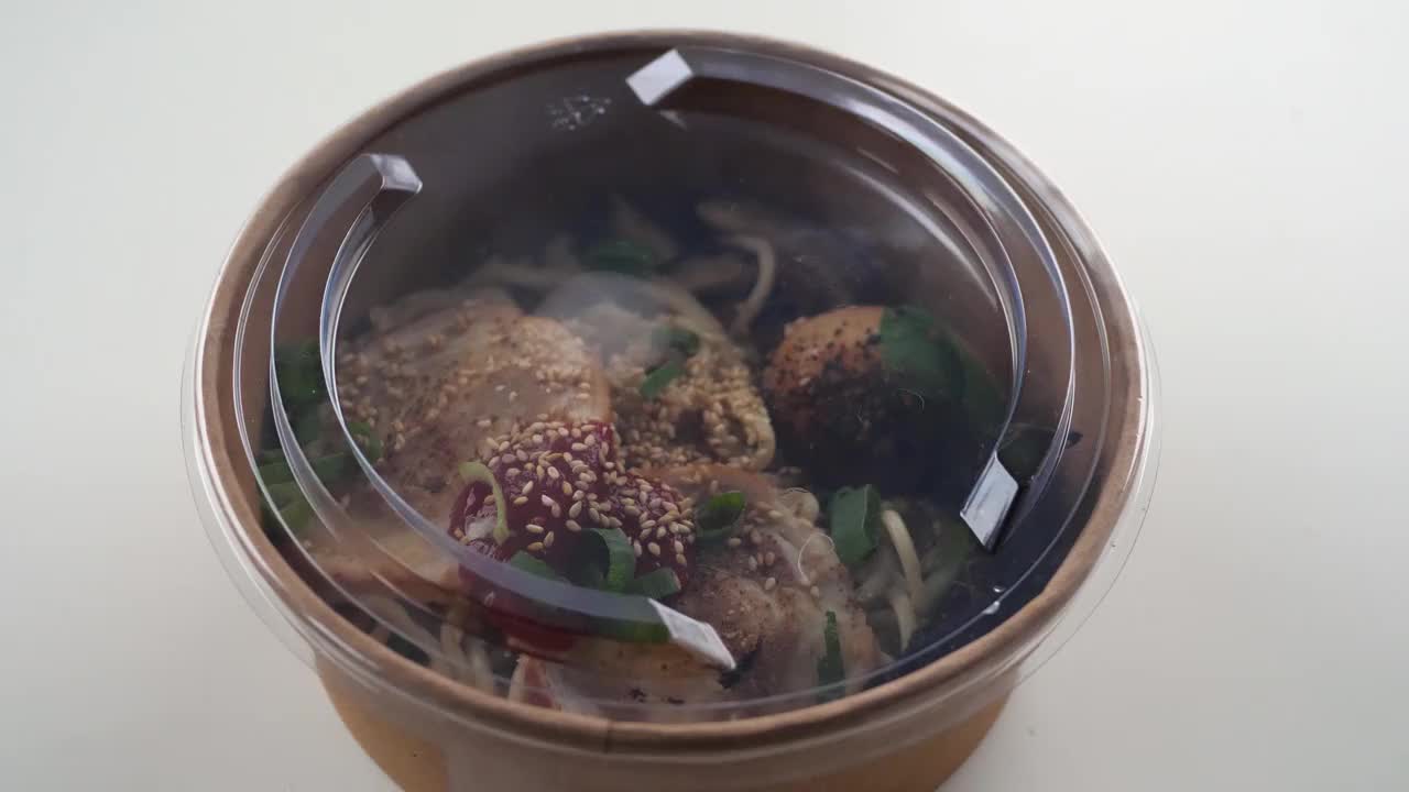 一位女士在一张白色的桌子上打开外卖拉面汤