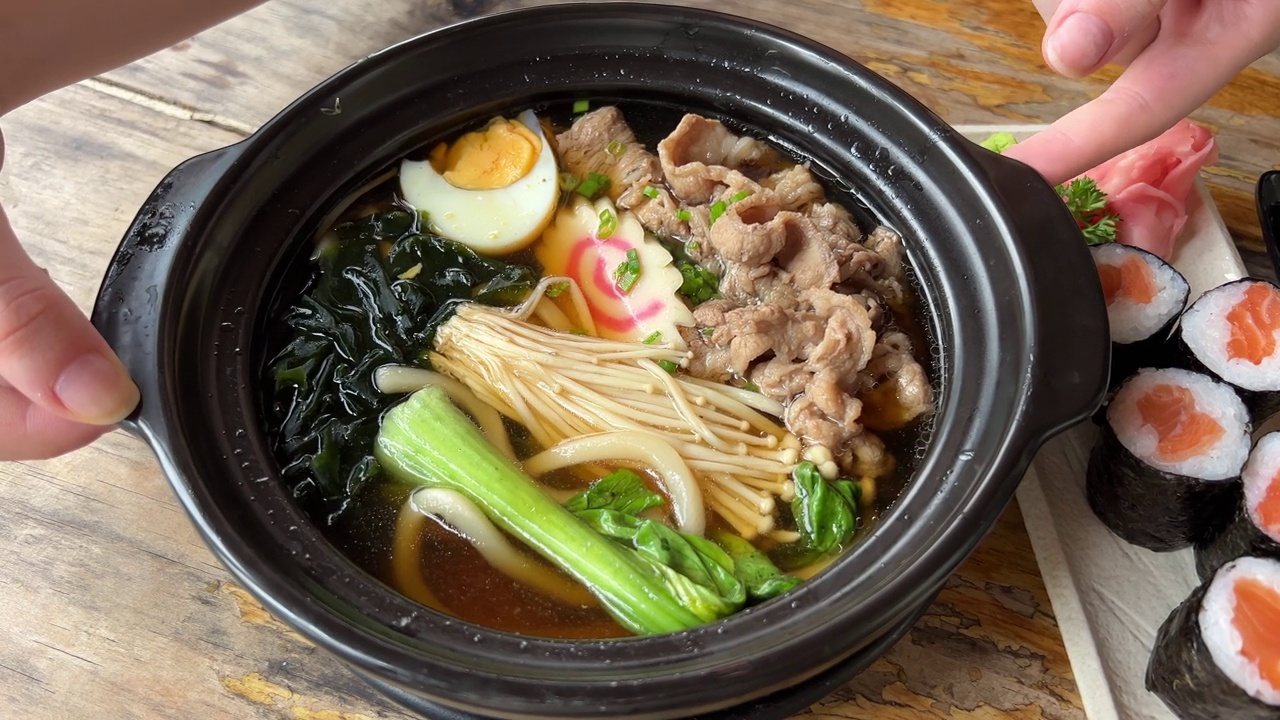 亚洲面条汤，拉面与鸡肉，豆腐，蔬菜和鸡蛋在一个黑色的碗。板岩的背景。前视图。