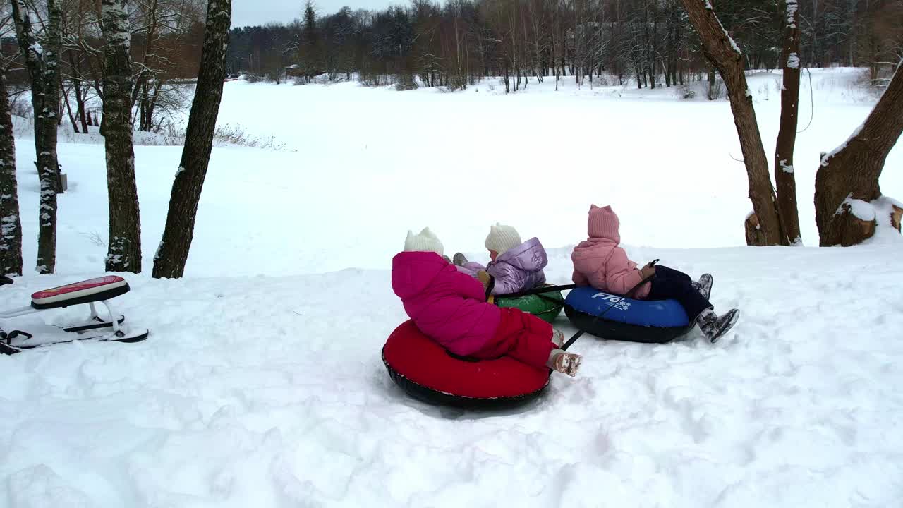 小孩子三胞胎姐妹在冬天骑在一个充气奶酪蛋糕与低雪坡